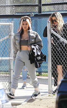 the two women are walking together in front of a fenced area and one is carrying a backpack