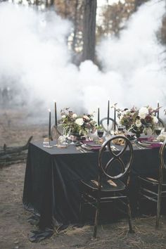 the table is set with black linens and candles for an elegant dinner party in the woods