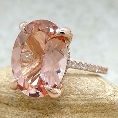 an oval shaped pink diamond ring on top of a rock with diamonds around the band