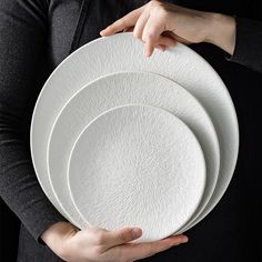 a person holding three white plates in their hands