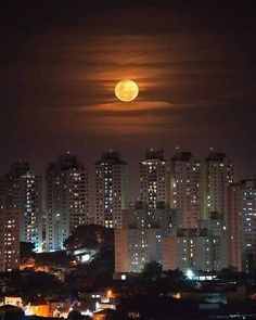 the full moon shines brightly in the night sky over some buildings and skyscrapers