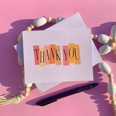 a thank you card sitting on top of a table next to some beads and a pen