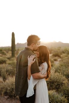 a man and woman kissing in front of a cactus field with the sun setting behind them