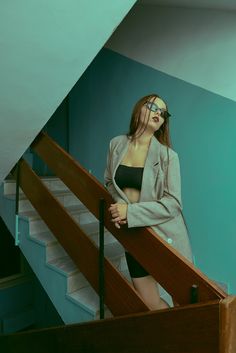 a woman standing on top of a stair case next to a wooden hand rail and blue wall