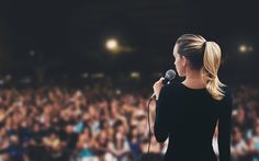 a woman speaking into a microphone in front of a large audience at a concert or conference