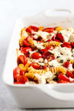 a white casserole dish filled with pasta, tomatoes and cheese covered in sauce