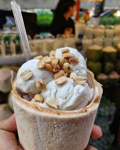 a person holding up a cup with ice cream and nuts on top in a store