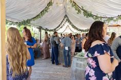 a group of people standing under a white tent next to a wooden barrel filled with wine