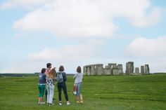 four people standing in front of stonehenge on a grassy field looking at the sky