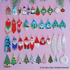 a collection of christmas themed earrings hanging on a pink wall next to a pine tree