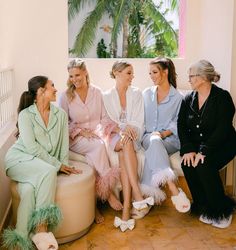 four women in robes sitting on a couch talking to each other and smiling at one another