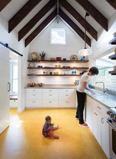 an open kitchen with white cabinets and wood beams on the ceiling, along with wooden flooring