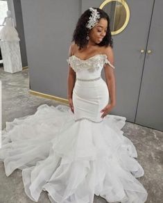 a woman in a white wedding dress standing next to a gray and gold wall wearing a tiara