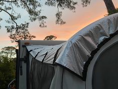 an rv parked under a tree with the sun setting in the back ground behind it