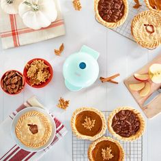 several pies are arranged on a table with apples and other desserts around them