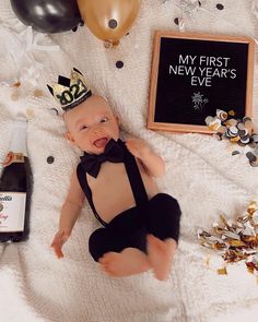 a baby wearing a black bow tie laying on top of a blanket next to balloons