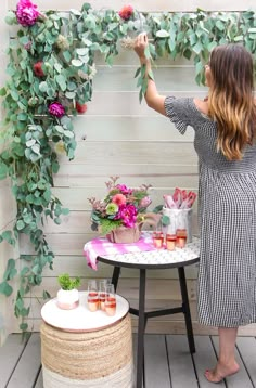 a woman standing in front of a table with flowers and drinks on top of it