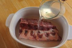 someone pours water into a bowl filled with meat that is sitting on a wooden table