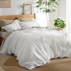 a bed with white sheets and pillows in a room next to a potted plant