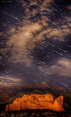 the night sky is filled with stars and clouds above a large rock in the foreground