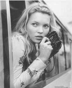 a woman holding a camera in her right hand and looking out the window at something