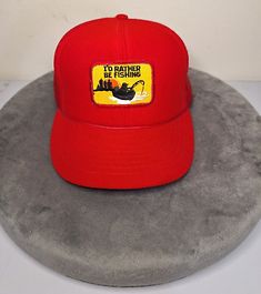 a red hat with the words to rather be fishing on it sitting on top of a rock