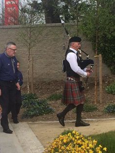 a man in a kilt playing bagpipes while people watch from the sidewalk