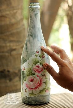 a hand is pointing at a painted glass bottle with flowers on the inside and outside