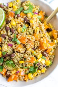 a white bowl filled with rice and veggies next to a lime wedge on the side