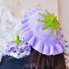 a woman wearing a crocheted hat with a cat laying on her back next to it