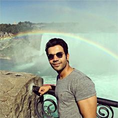 a man standing in front of a waterfall with a rainbow