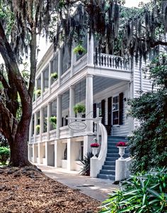 a white house with lots of trees and plants on the front porch, surrounded by spanish moss