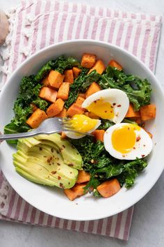 a bowl filled with vegetables and eggs on top of a striped napkin next to a fork