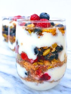 two glasses filled with fruit and yogurt on top of a marble countertop