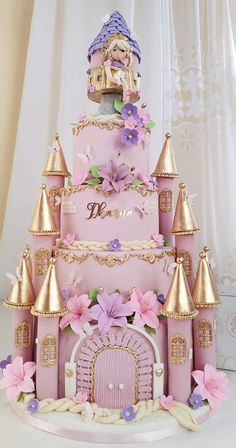 a pink castle cake with purple flowers on the outside and gold trimmings around it