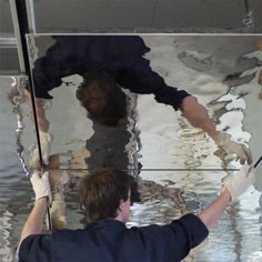 a man is cleaning the glass in front of a mirror that reflects another man's reflection