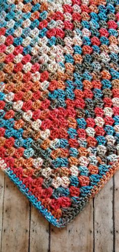 a multicolored crocheted blanket laying on top of a wooden floor