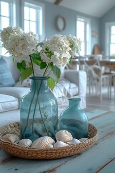 two vases filled with white flowers sitting on top of a table next to shells