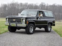 a black truck parked on top of a gravel road next to a lush green field