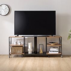 a flat screen tv sitting on top of a wooden shelf next to a plant and a clock