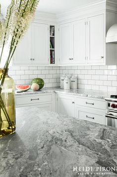 a kitchen with marble counter tops and white cabinets, along with flowers in a vase