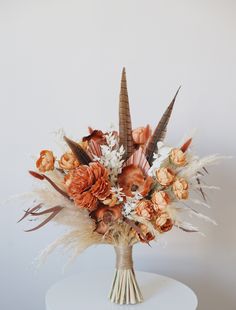 a vase filled with flowers and feathers on top of a white table next to a wall