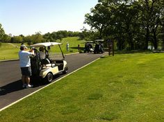 a golf cart driving down the road with people on it and carts in the background