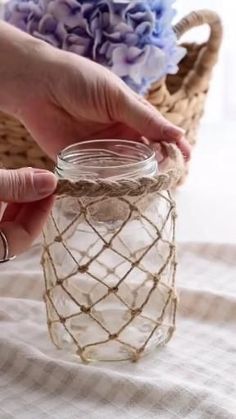 a person is holding a glass jar with rope around it and flowers in the background