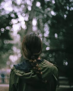 a woman standing in front of trees with her back to the camera