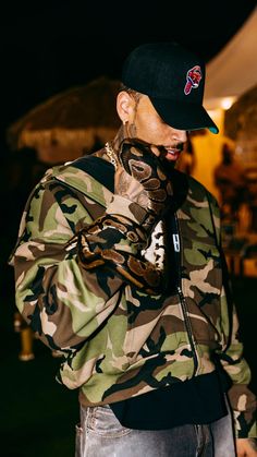 a man with a snake on his arm wearing a baseball cap and camouflage print jacket