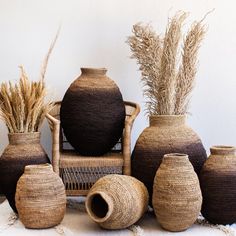 several vases with grass in them sitting on a table next to a wicker chair