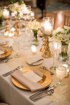 the table is set with white and gold plates, silverware, candles and flowers