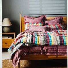 a bed with colorful blankets and pillows in a room next to a night stand on the floor