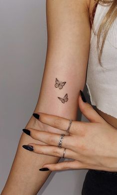 two women with matching rings and butterfly tattoos on their arms, both holding each other's hands